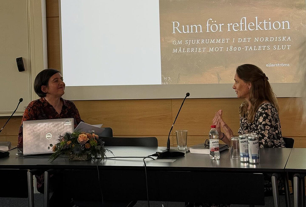 Petra och opponenten sitter vid katedern och samtalar. Foto.