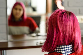 Bild på rödhårig tjej bakifrån som ittar sig ibspegeln så att man ser hennes spegelbild.