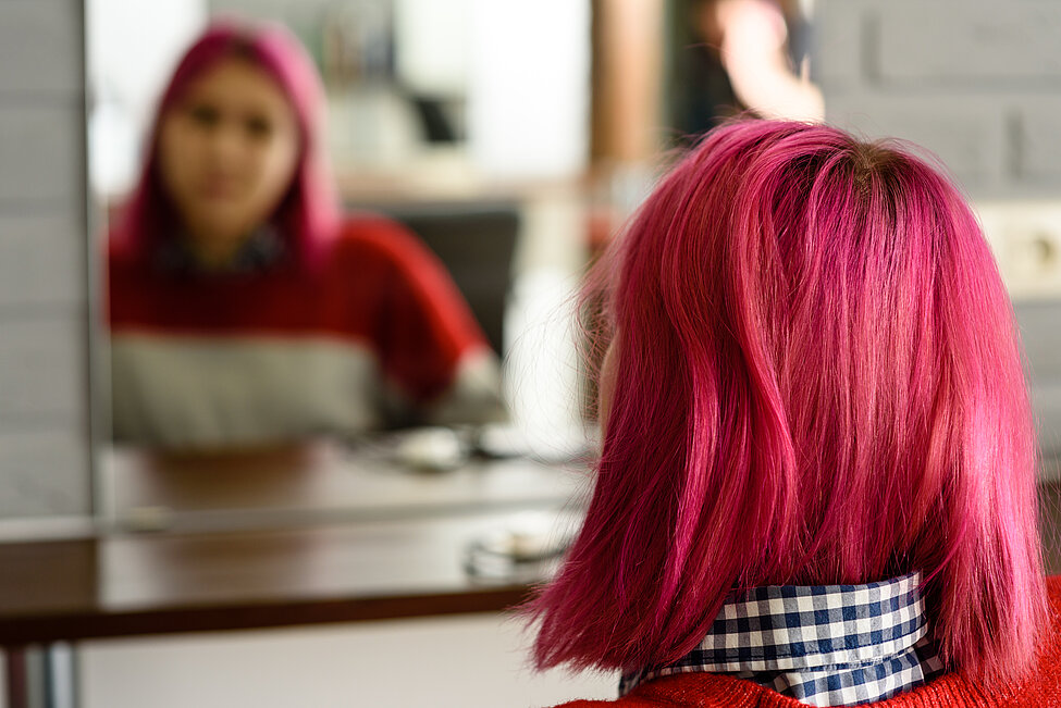 Bild på rödhårig tjej bakifrån som ittar sig ibspegeln så att man ser hennes spegelbild.