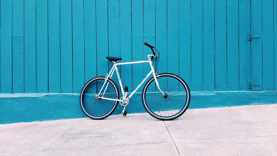 En cykel står lutad mot en blå vägg. Foto.