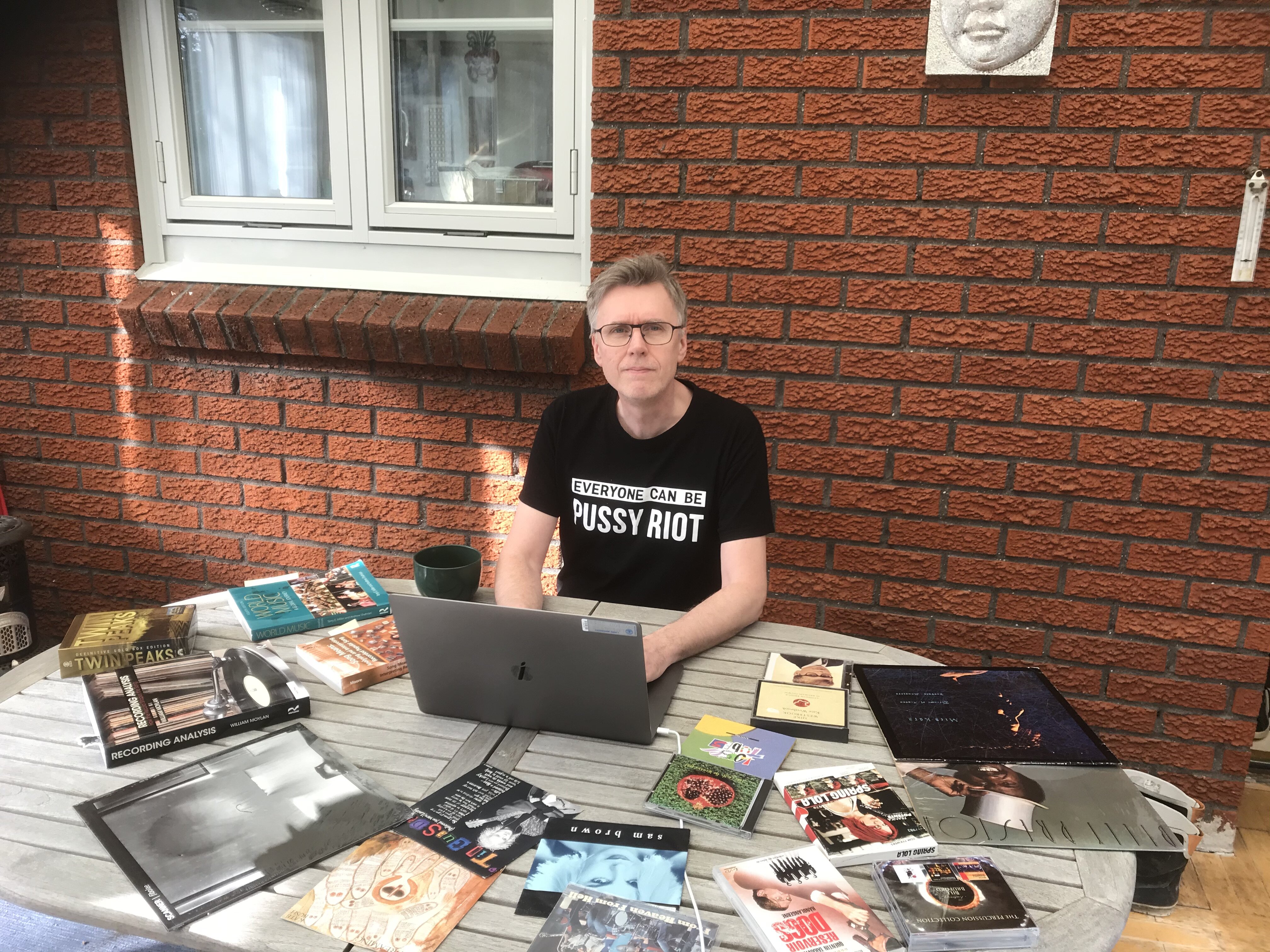 En person sitter vid ett bord och jobbar vid en dator. På bordet ligger böcker utspridda.