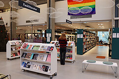 En flicka står med ryggen mot fotografen och tittar i en bokhylla i ett folktomt bibliotek. Foto.