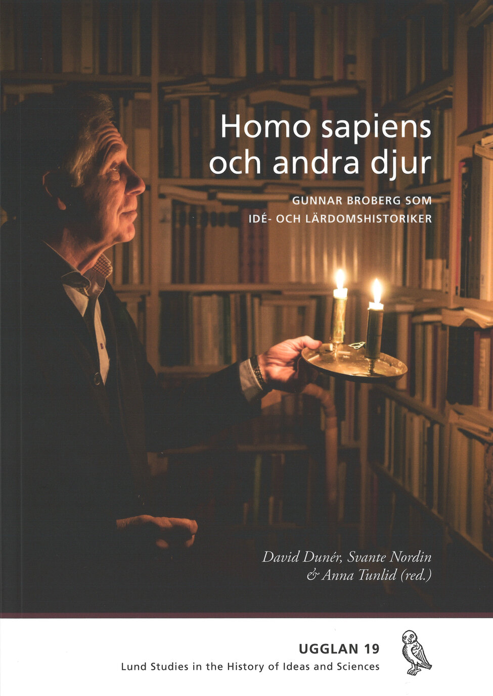 Omslagsbild. Gunnar Broberg lyser upp sin bokhylla med en ljusstake med två stearinljus. Foto.