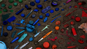 Plastföremål i olika färger utplacerade på ett underlag av sand.