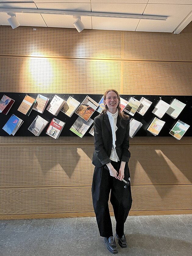 Sarah står framför spikbrädan med avhandlingar. Foto.