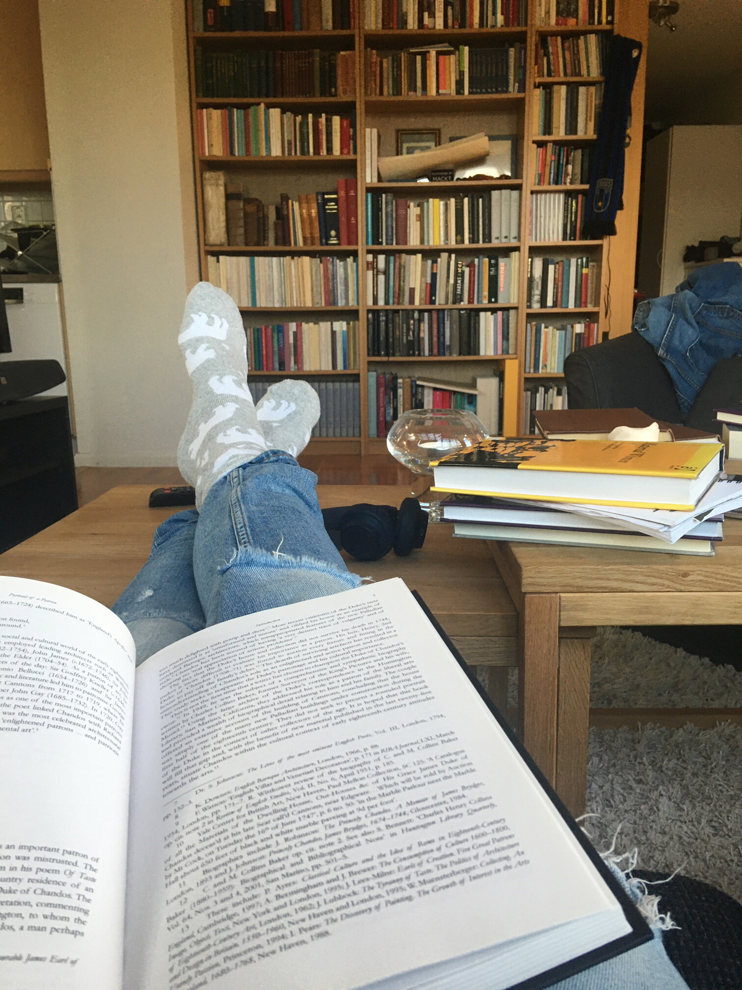 Person sitter i en soffa med en bok i knät och fötterna på bordet