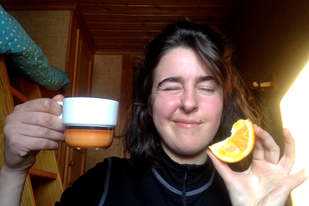 Person med kaffekopp i ena handen och en apelsinklyfta i andra handen som blinkar mot kameran.