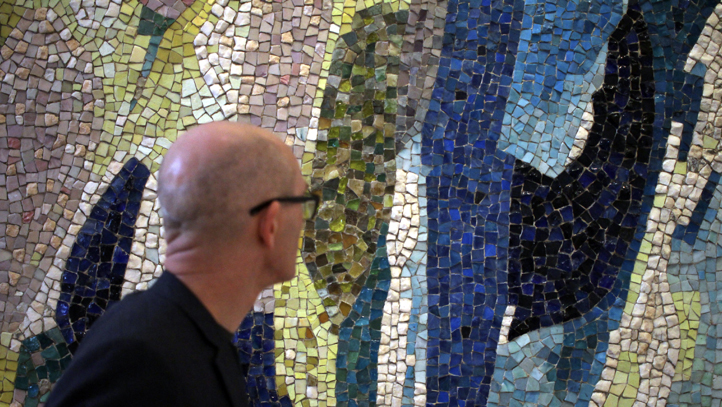 En man framför en tavla av mosaik